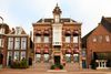 Front view of a historic brick hotel building with decorative architecture, large windows, and burgundy awnings. The hotel stands between neighbouring buildings along a city street.
